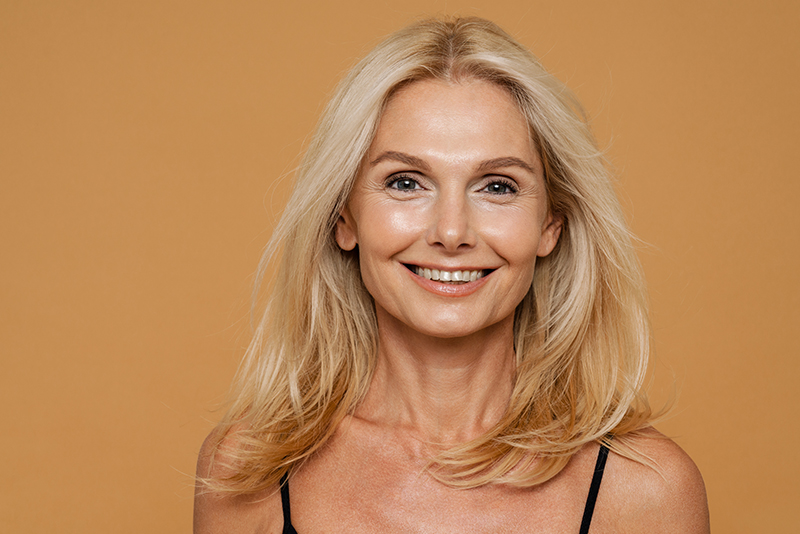 Mature blond beautiful woman wearing bodysuit smiling and posing at camera isolated over yellow background